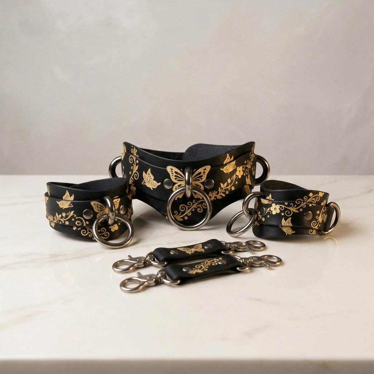 A set of black leather straps with gold floral designs, including butterfly motifs, arranged on a white marble surface.