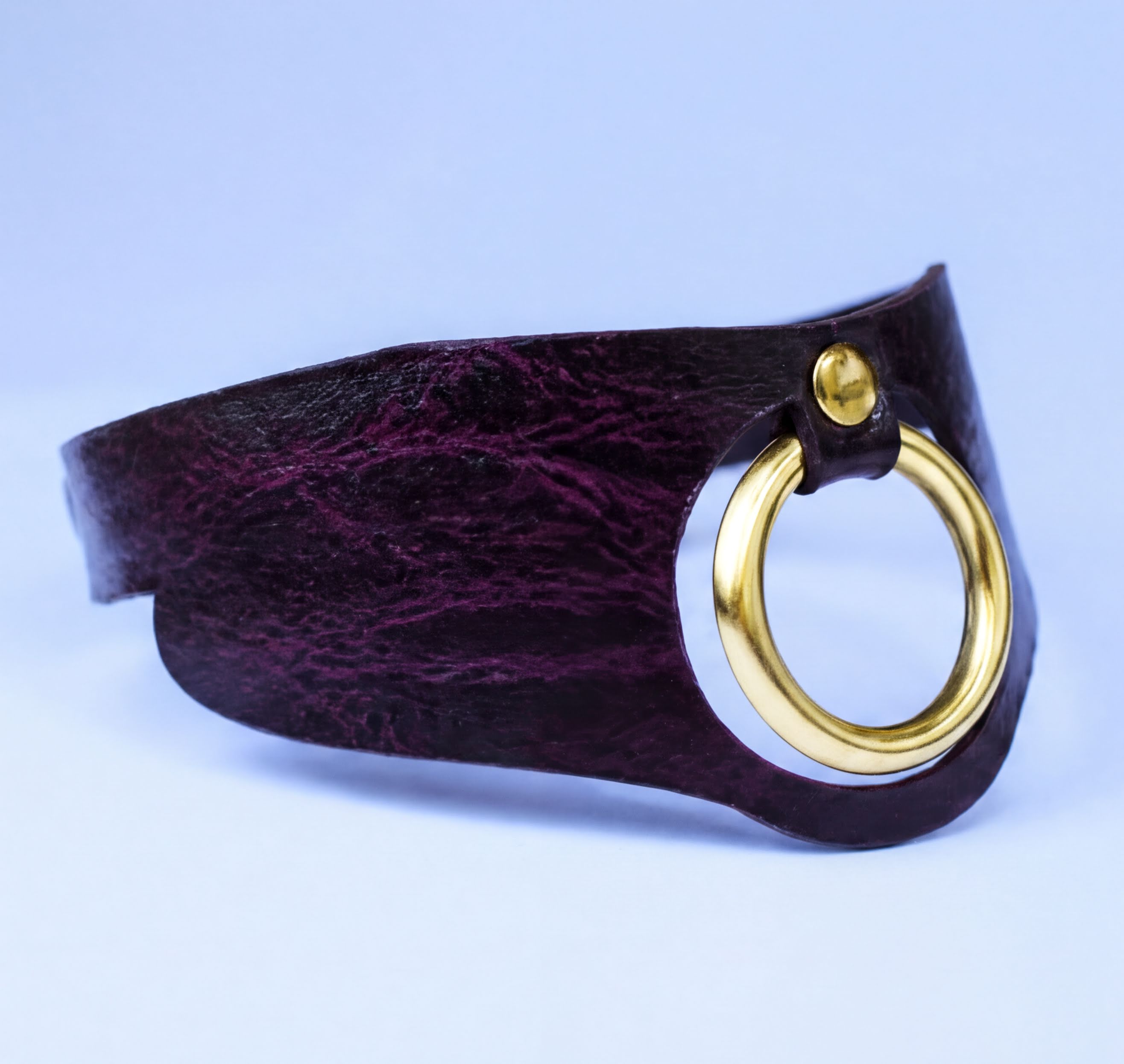 A close-up image of a dark purple leather choker necklace with a gold-colored circular clasp.