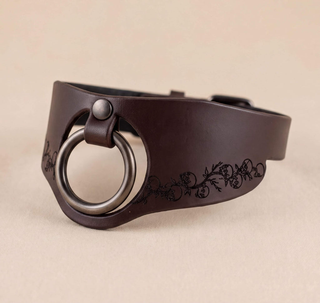 A brown leather choker necklace with a metal ring and a decorative floral pattern on the side.