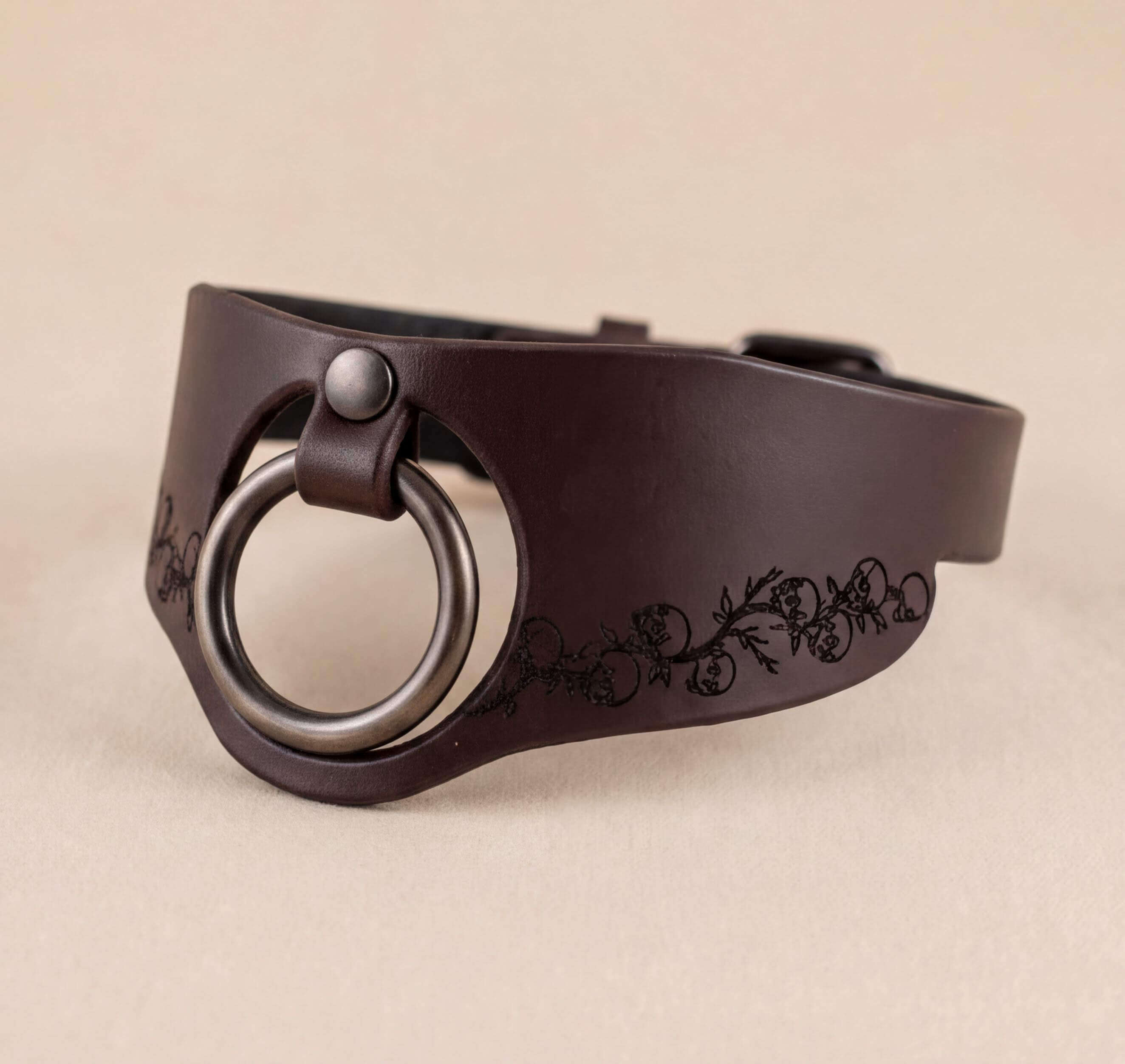 A brown leather choker necklace with a metal ring and a decorative floral pattern on the side.
