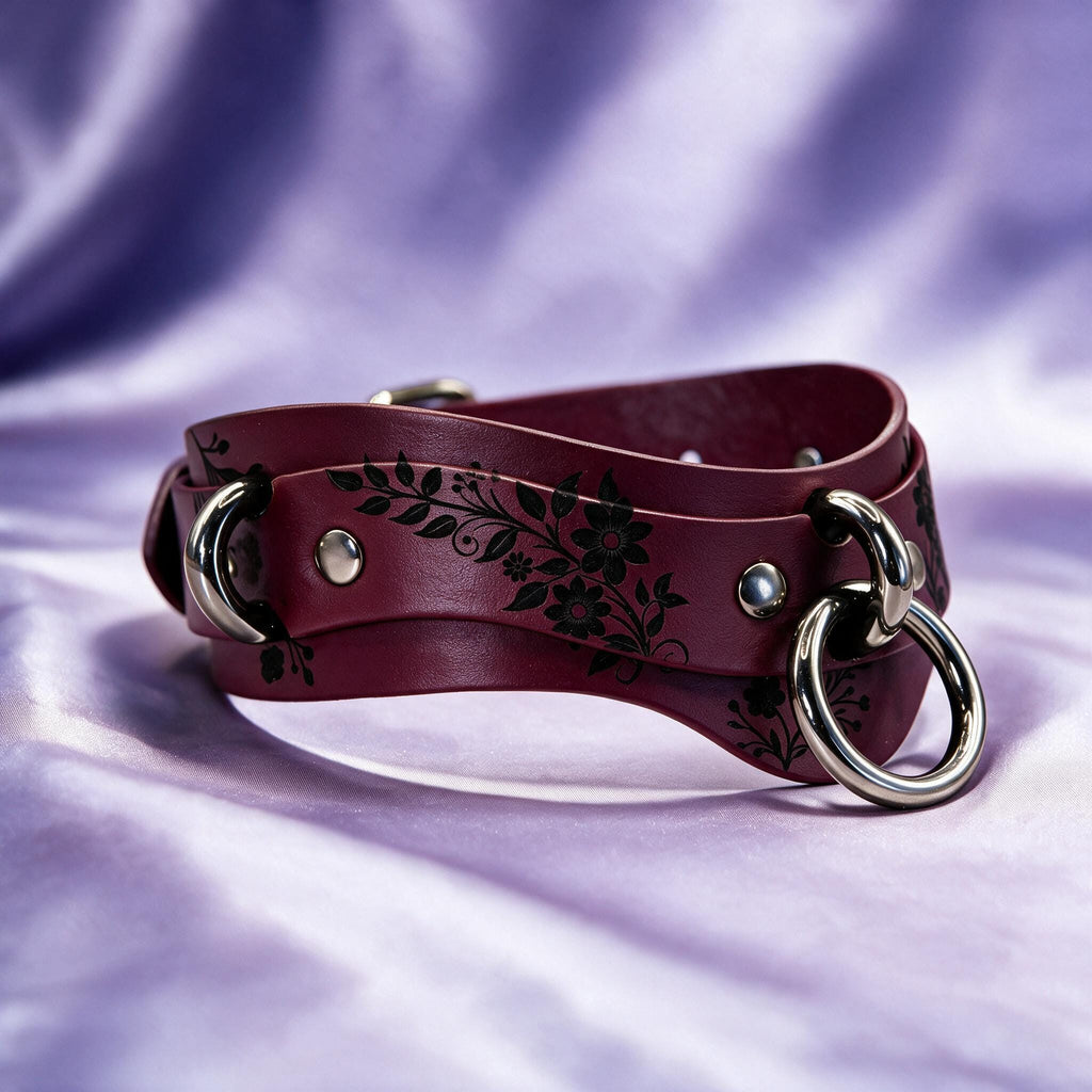 A burgundy leather belt with a floral design and metal rings is displayed against a purple background.