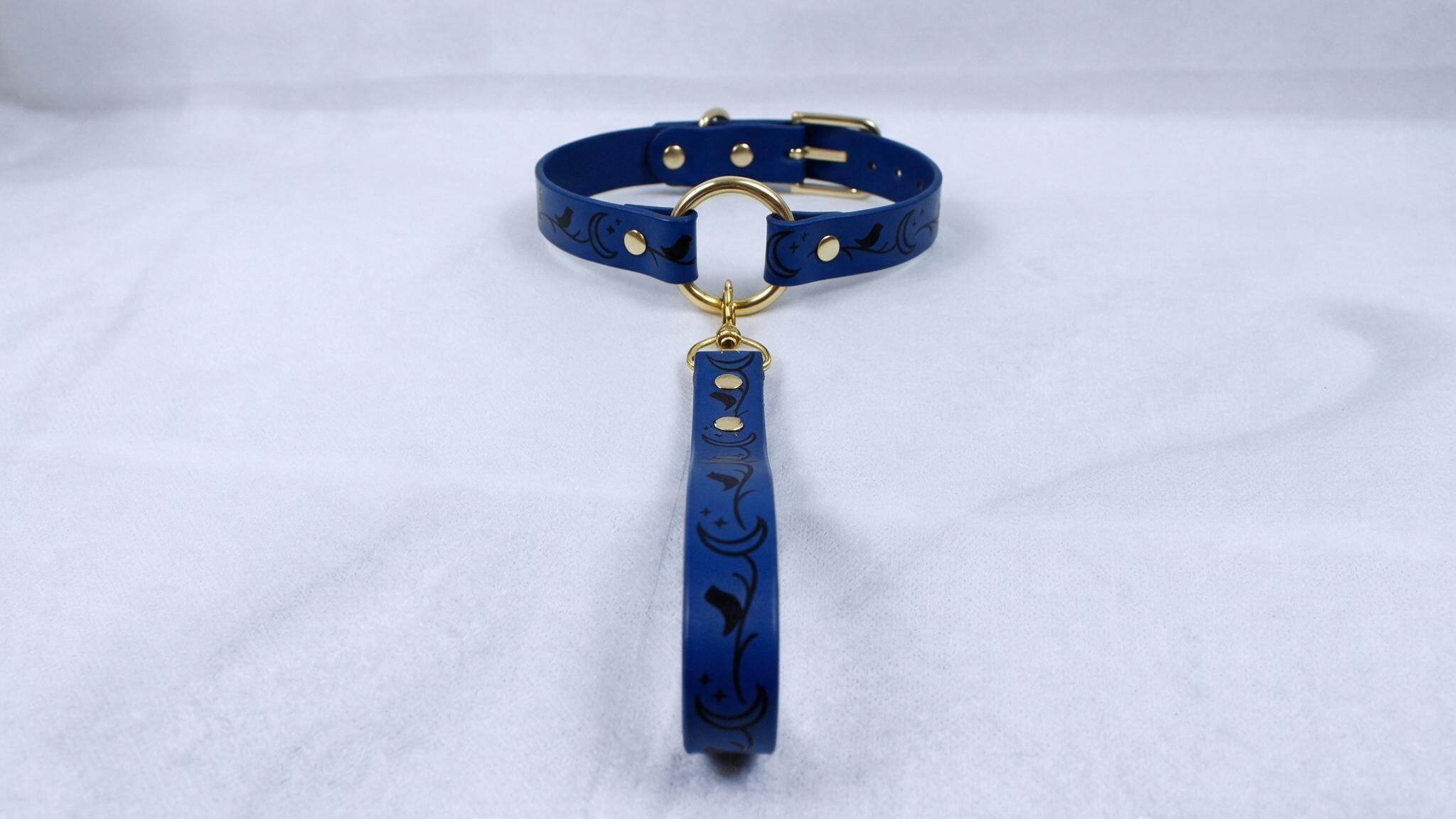 A blue collar with a gold buckle and a black floral pattern on the strap is displayed against a white background.