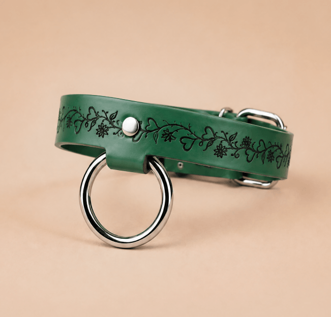 A green leather collar with a metal ring and floral designs on it.