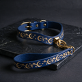 A blue leather dog collar with gold star and crescent designs, and a matching leash, both resting on a dark surface.