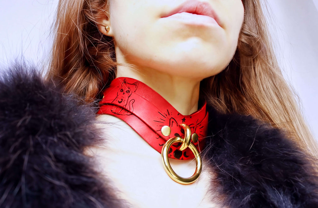 A close-up of a person wearing a red choker necklace with a gold ring, and a black fur coat.
