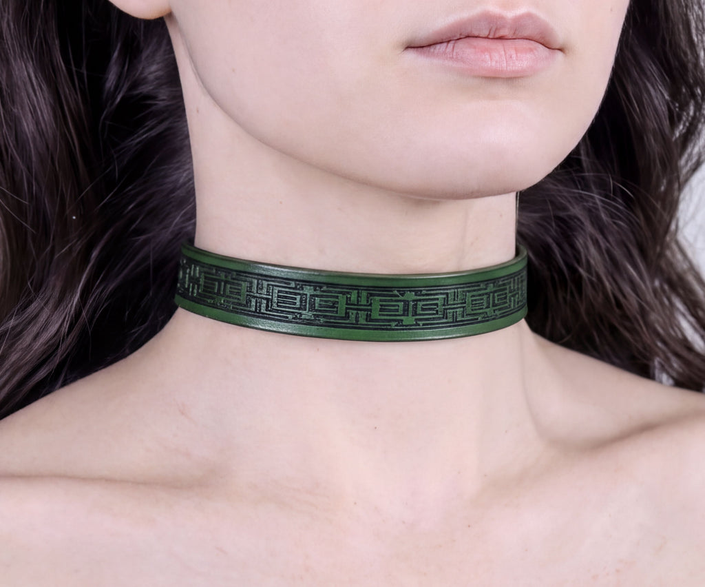 A close-up of a person's neck wearing a green choker necklace with a black geometric pattern.