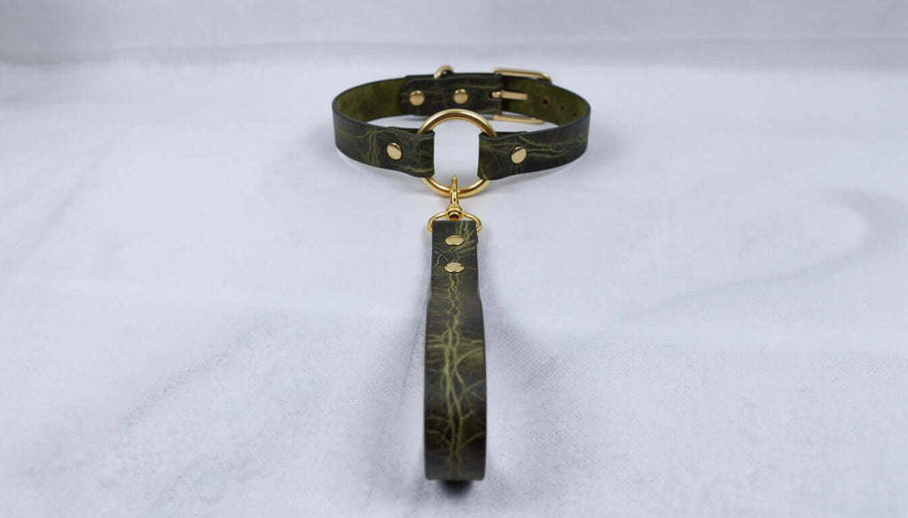 A dark green leather collar with a gold-colored buckle and a matching leash attached to it, resting on a white surface.