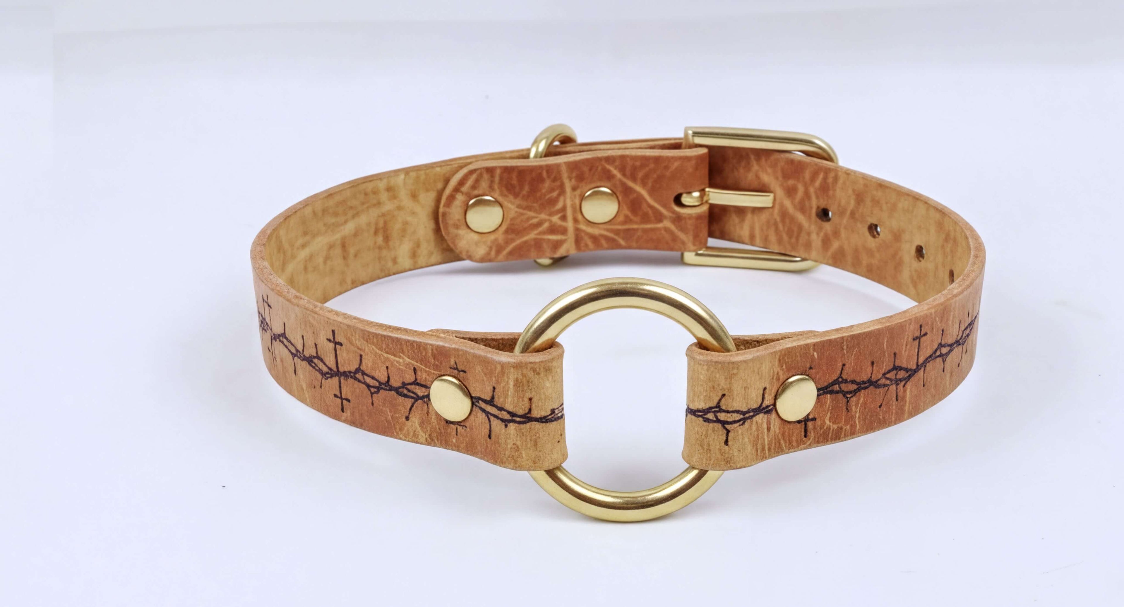A tan leather choker collar with a gold metal ring and a decorative pattern on the leather.