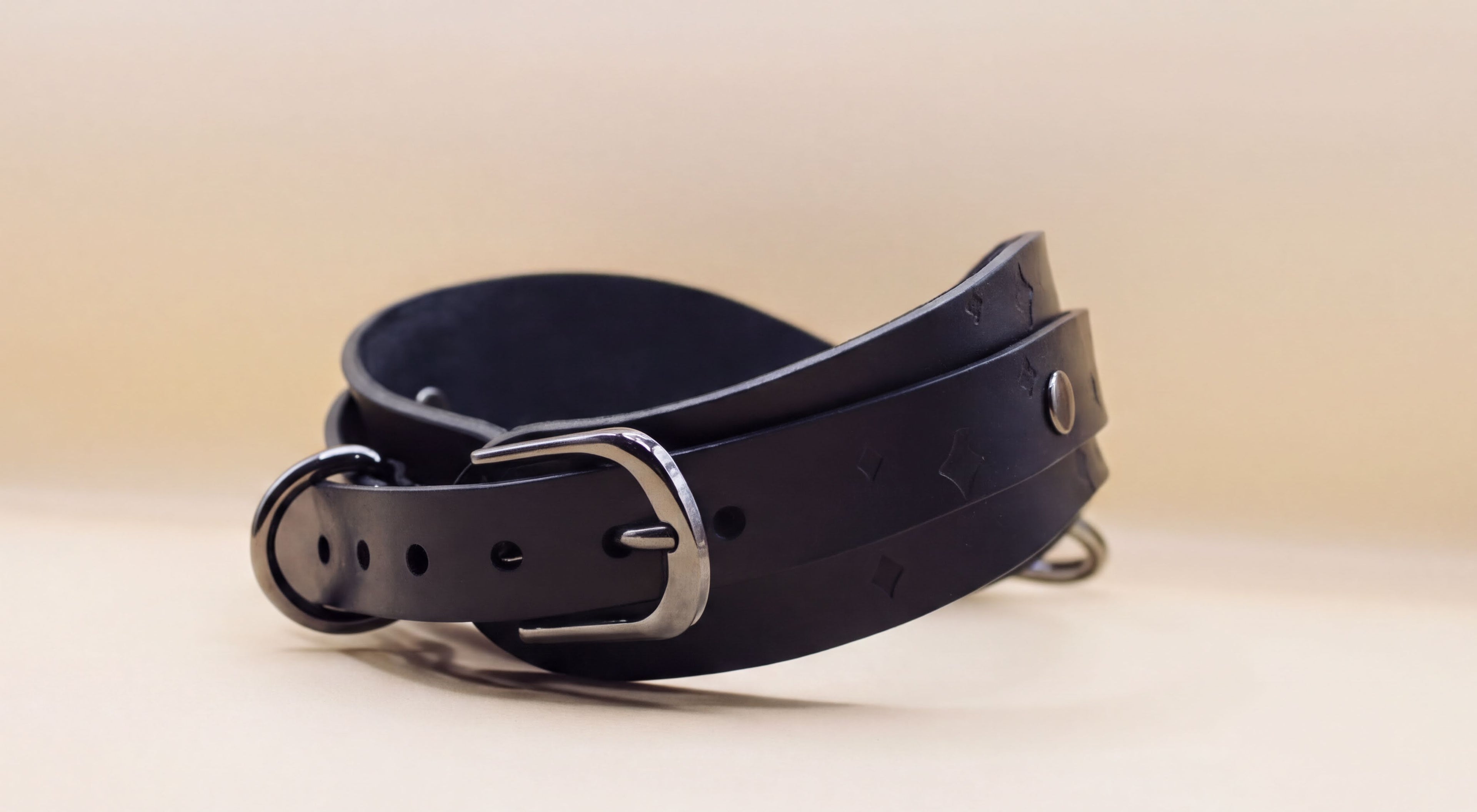 A black leather belt with a silver buckle is shown against a light beige background.