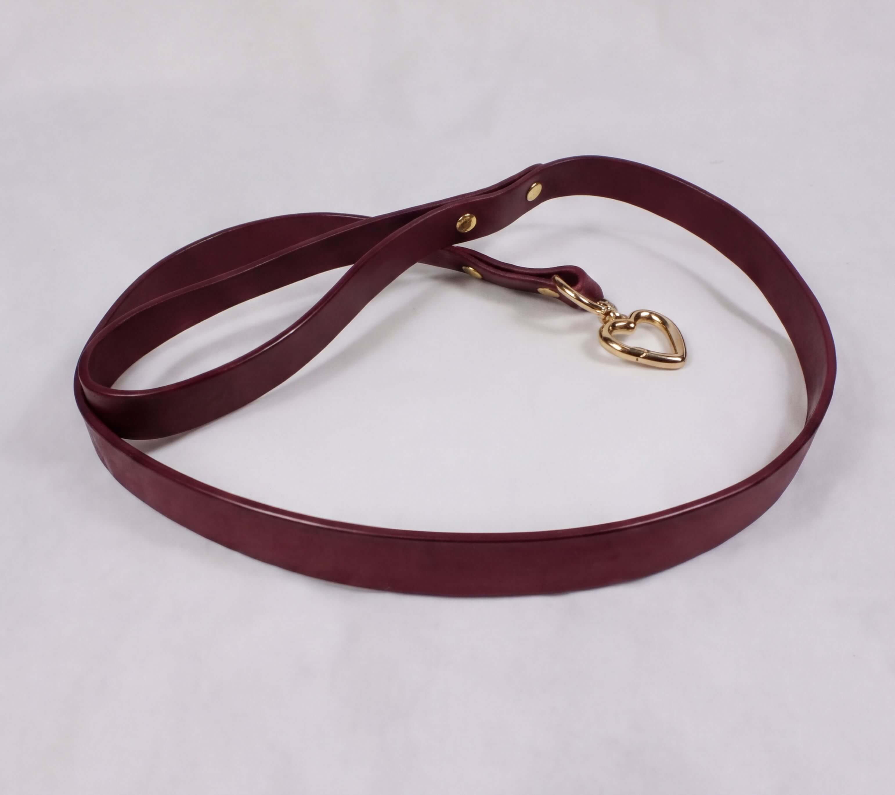 A burgundy leather dog leash with a gold heart-shaped charm attached.