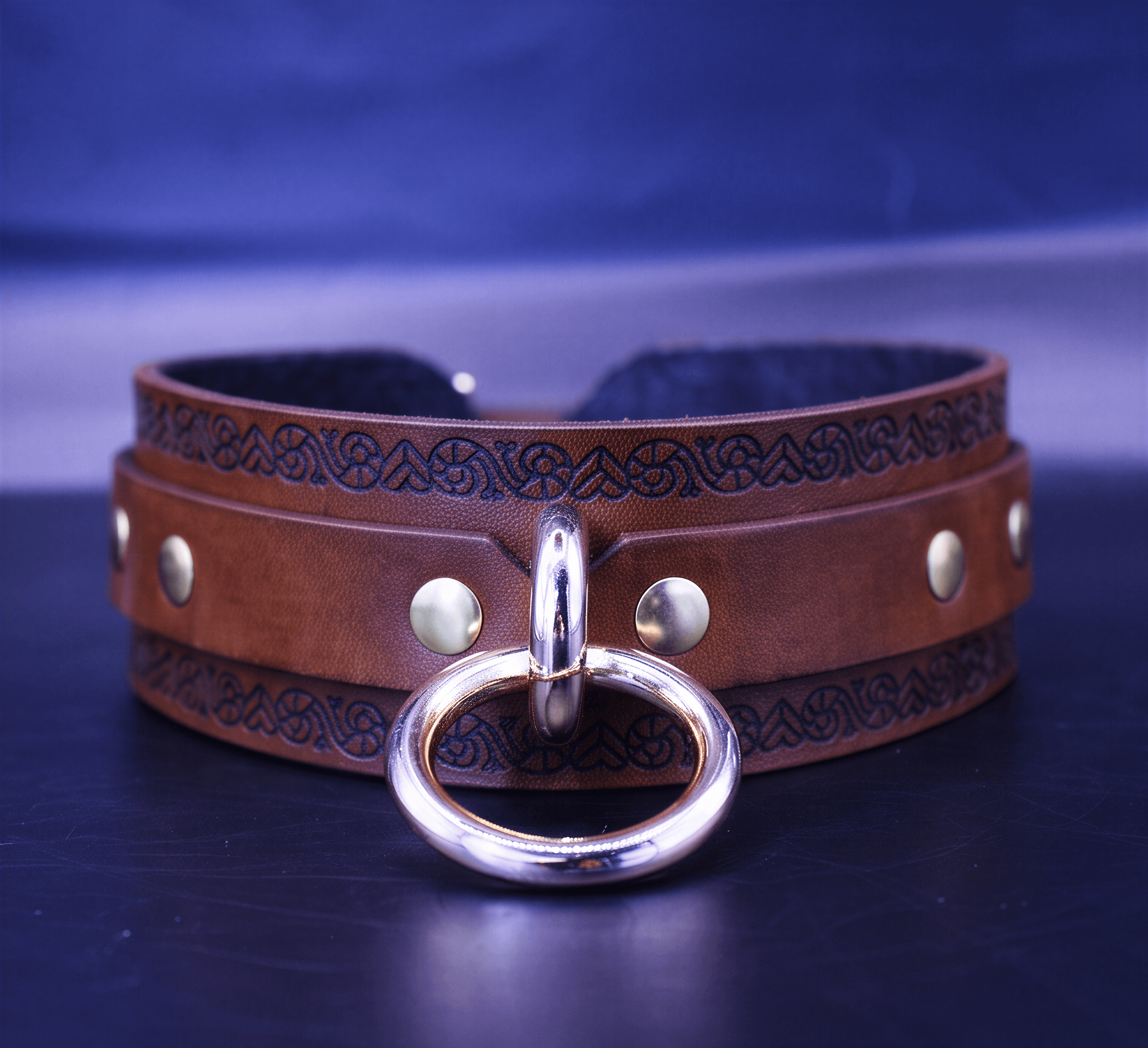 A brown leather choker necklace with a metal ring and decorative elements on the band.