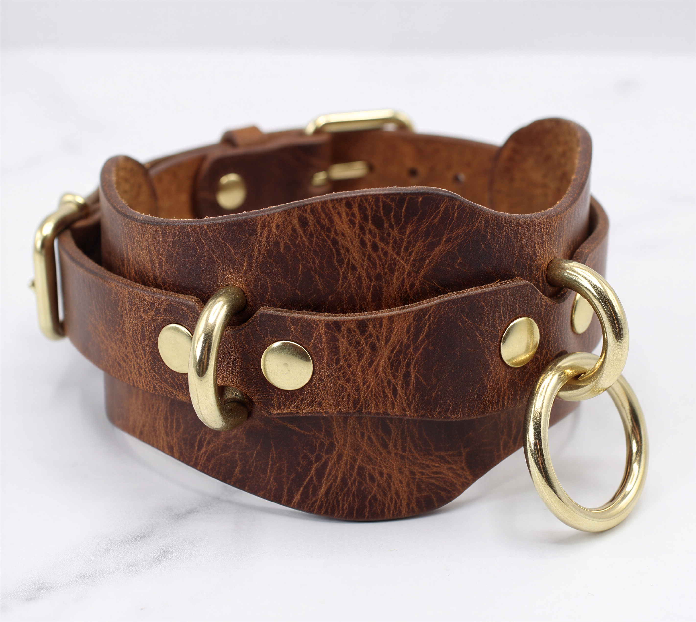 A brown leather choker necklace with brass-colored metal rings and a buckle-style clasp.