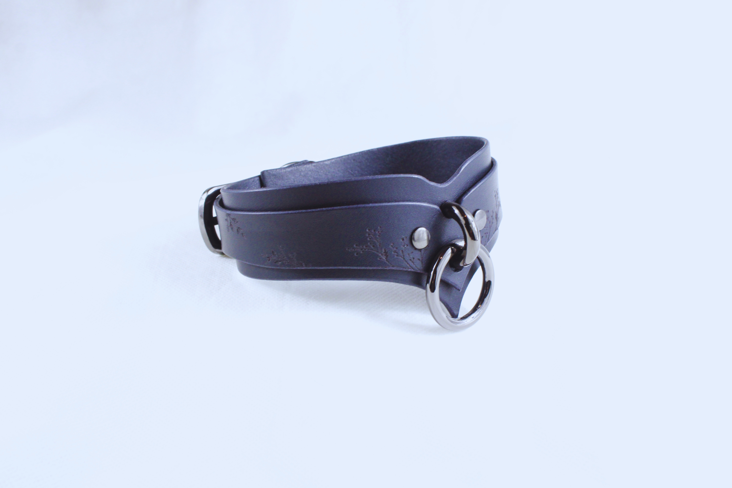 A dark blue leather choker necklace with metal rings and a buckle.