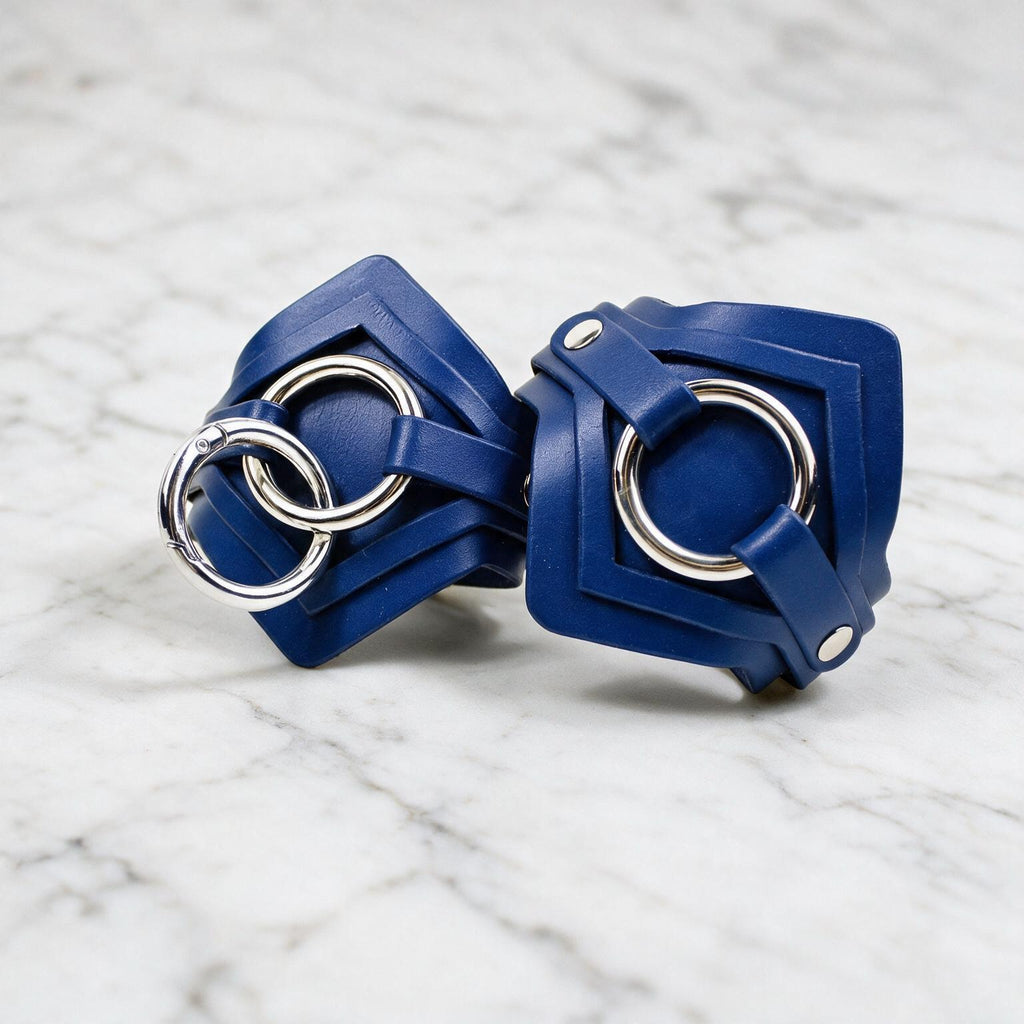A pair of blue leather cuffs with metal rings on them, placed on a marble surface.