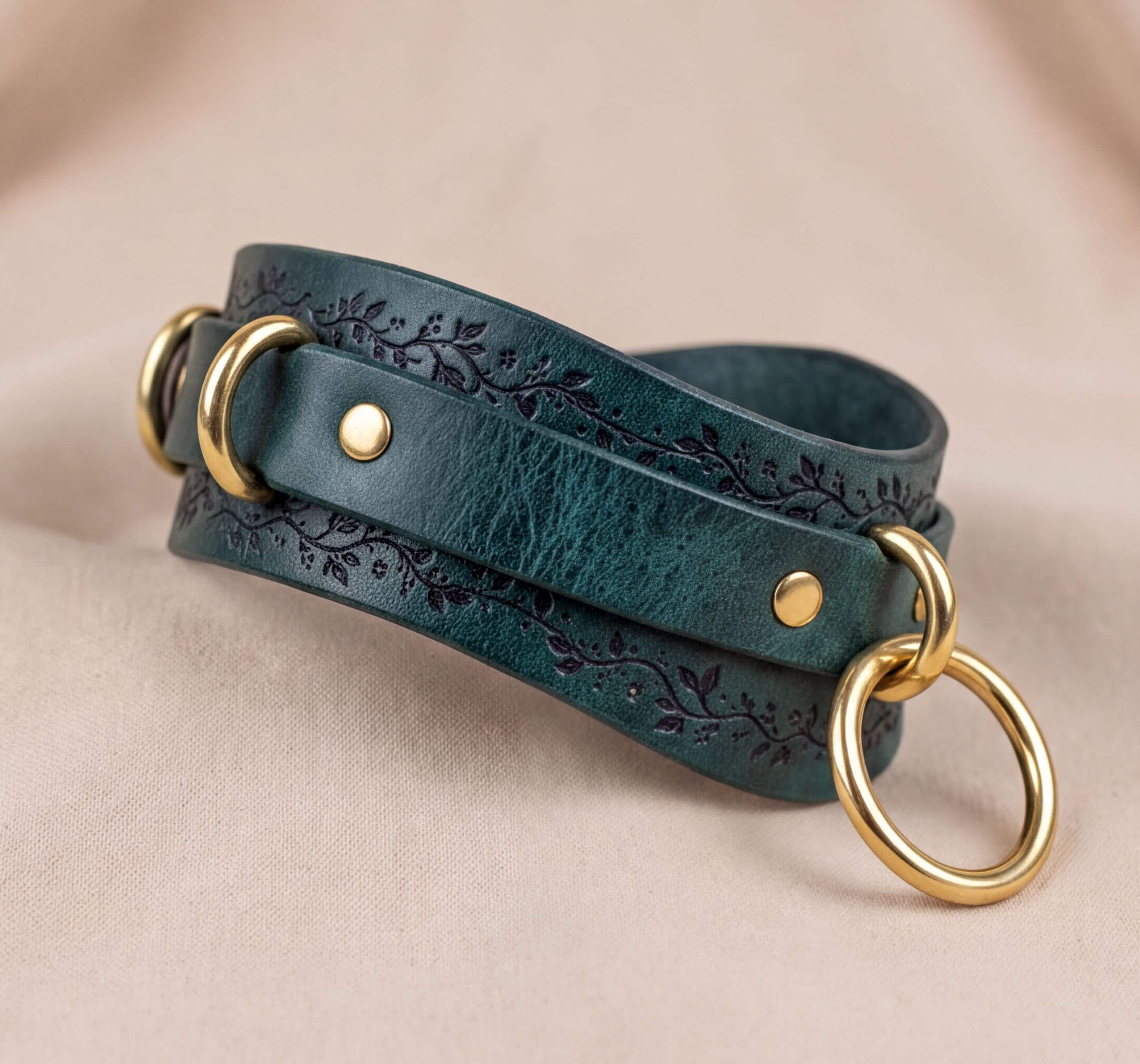 A green leather choker necklace with gold-colored metal rings and a decorative floral pattern on the leather.