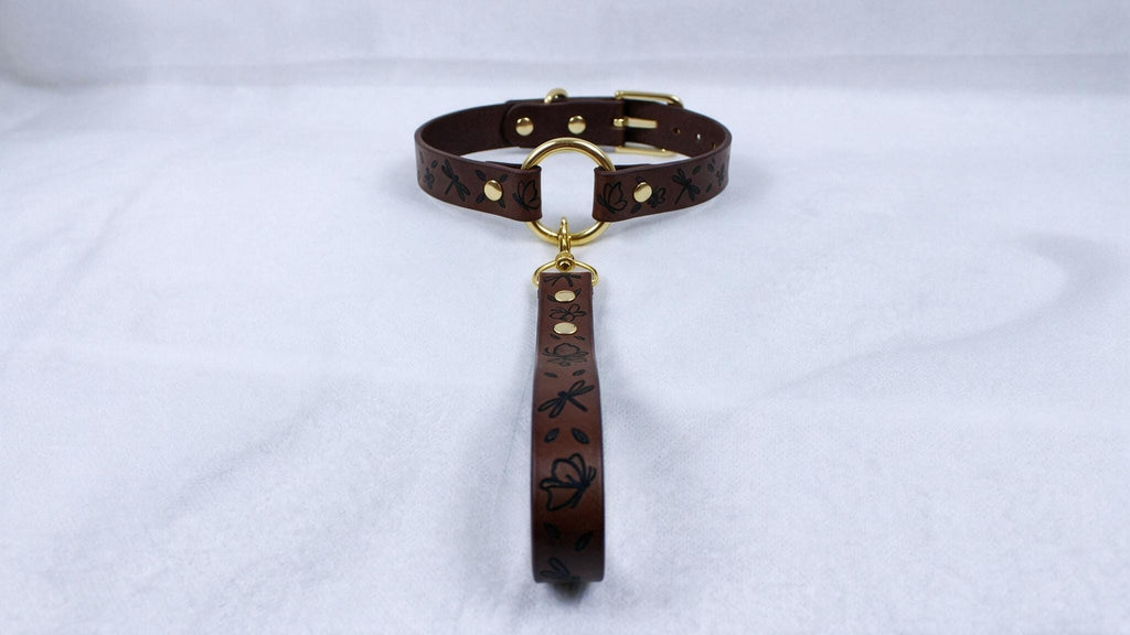 A brown leather collar with a gold buckle and a black floral pattern on the strap.
