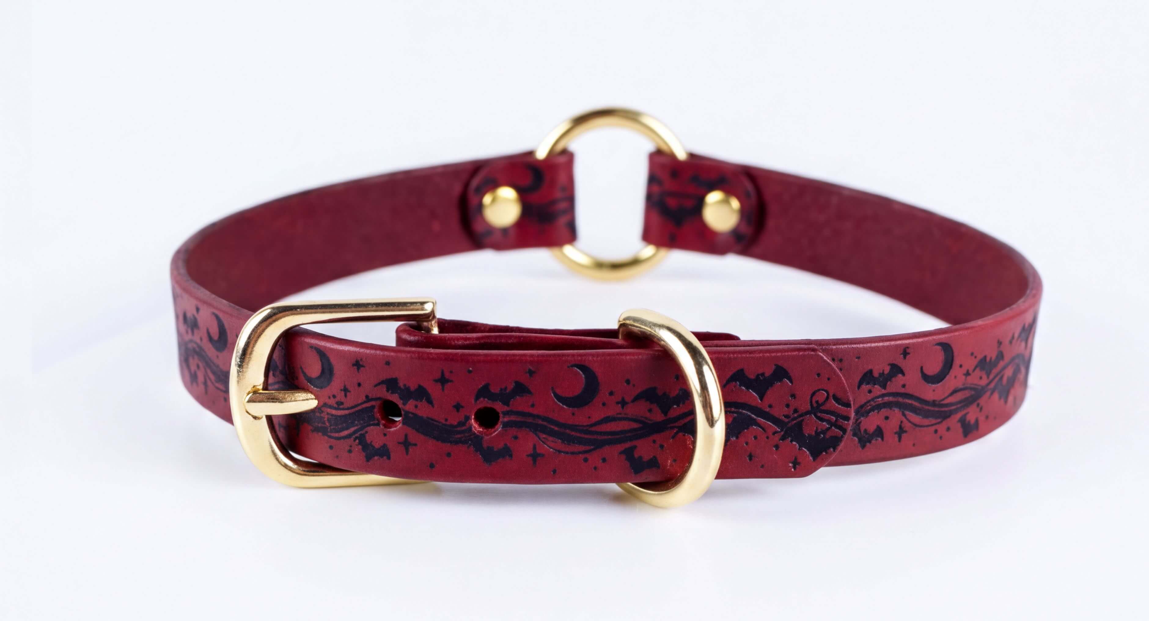A burgundy leather collar with a gold buckle and a black bat and moon design.