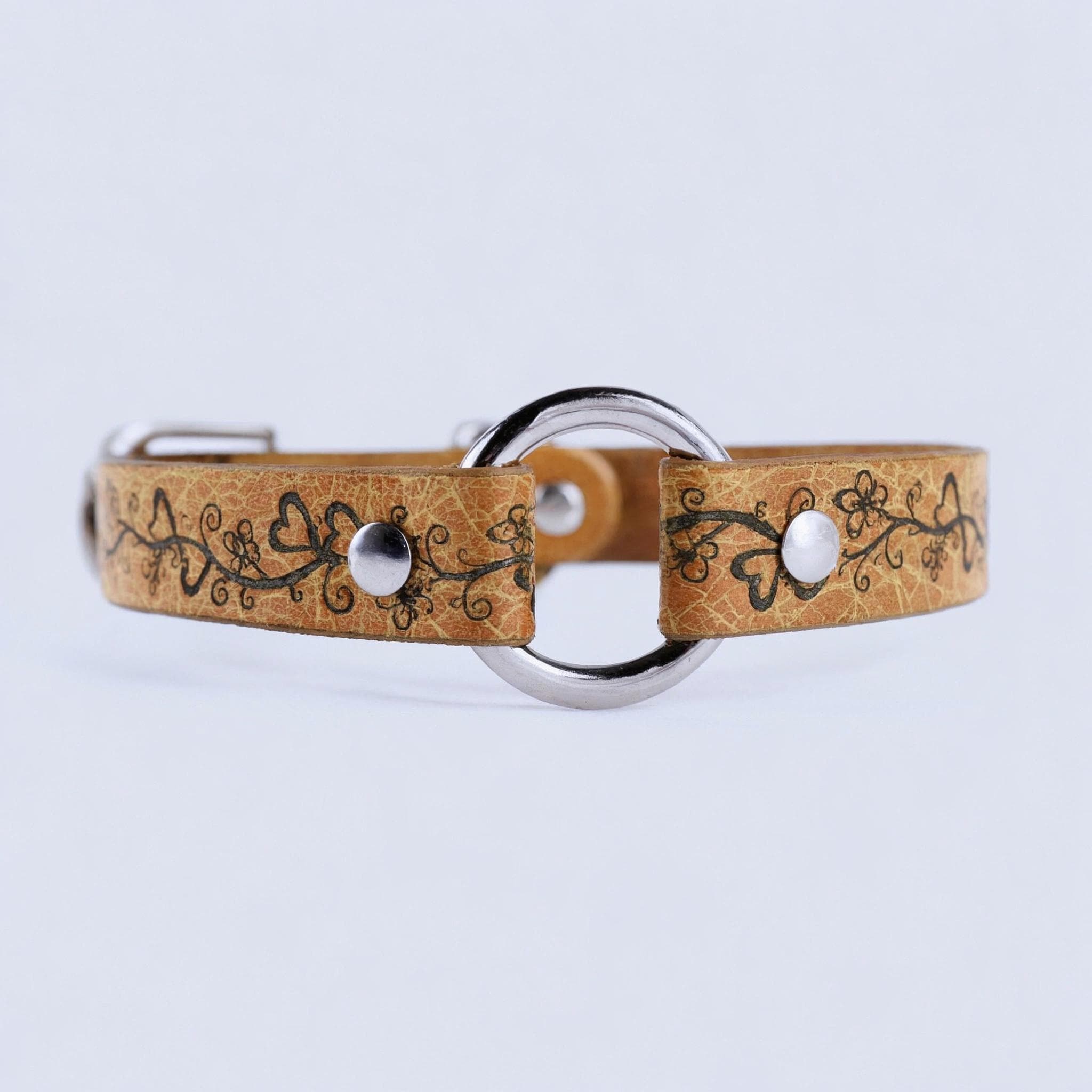 A tan leather collar with a floral design and metal ring, featuring two silver buttons.