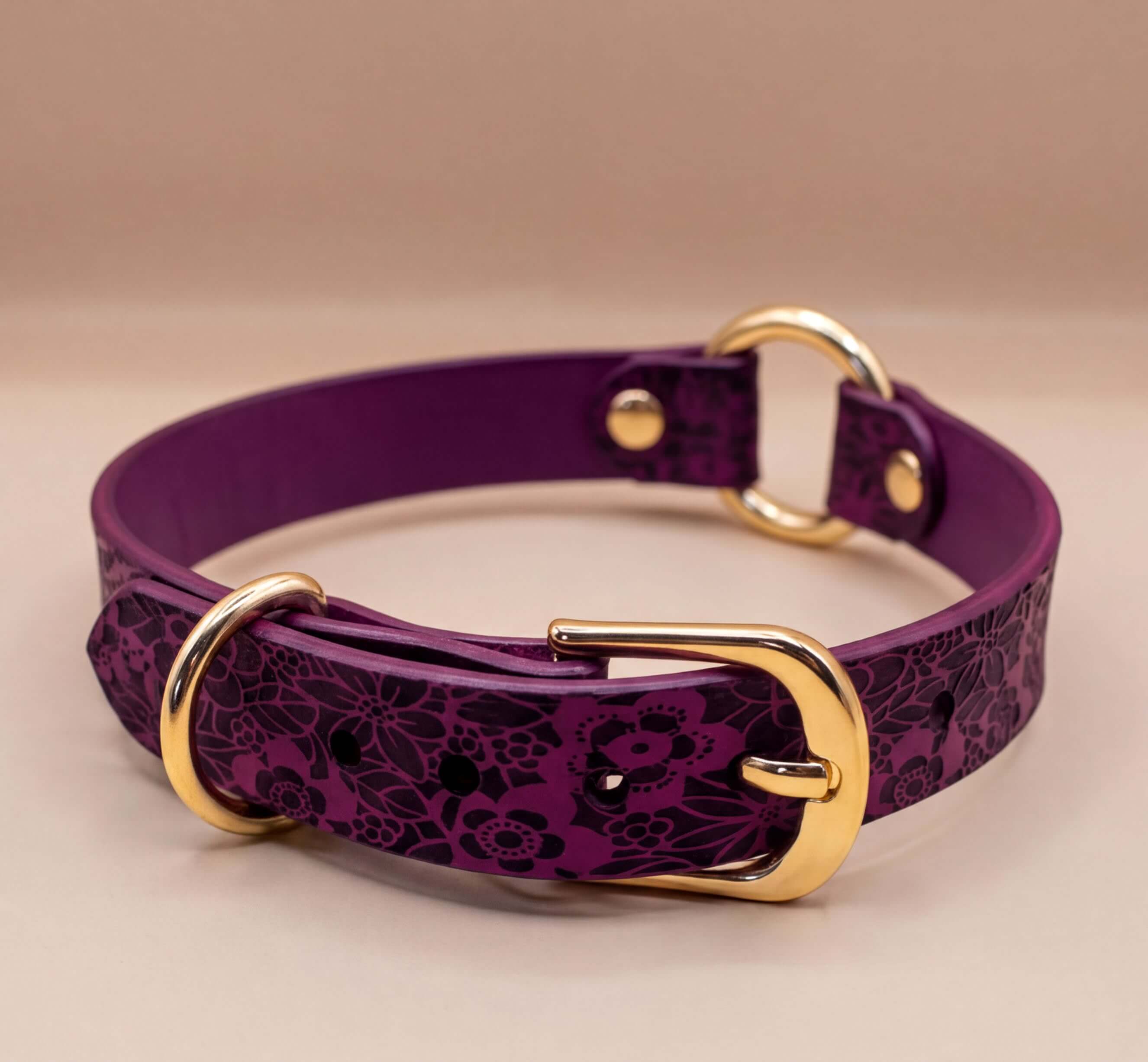 A purple leather dog collar with a floral pattern and two gold-colored buckles.