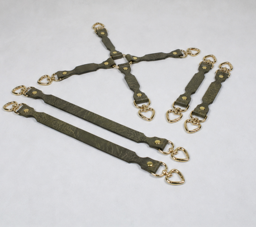 a collection of leather straps with gold-colored metal hardware, including heart-shaped buckles, arranged in various orientations.