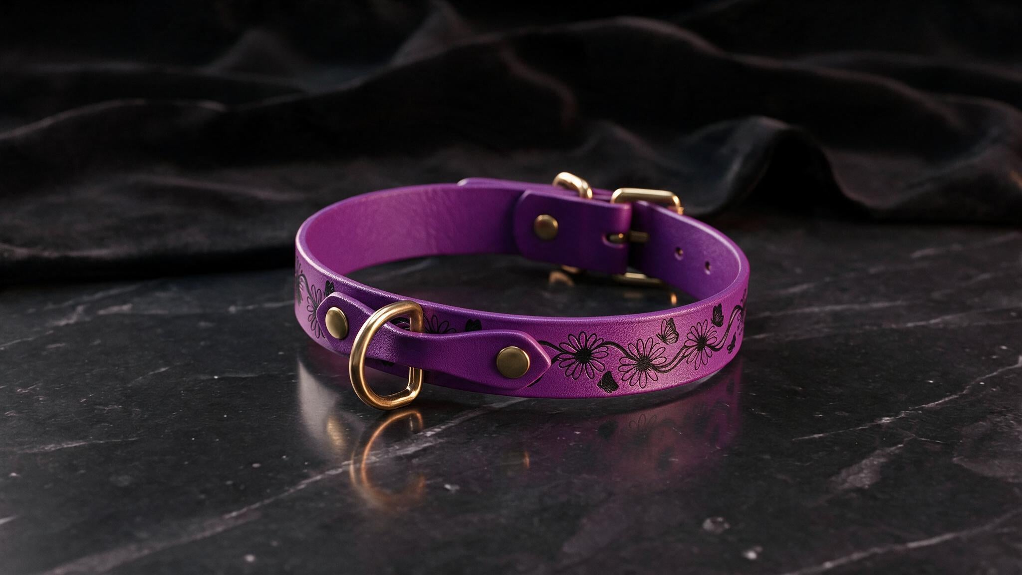 A purple leather collar with a floral design and gold hardware is displayed on a black marble surface.