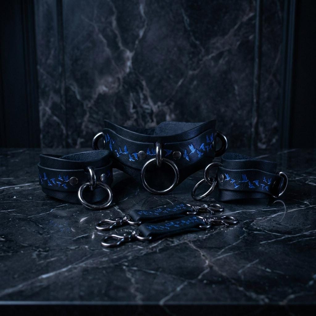 A set of black leather choker necklaces with blue bird designs, displayed on a dark marble surface.