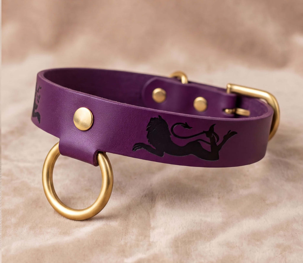 A purple leather dog collar with a lion design and gold-colored metal rings.