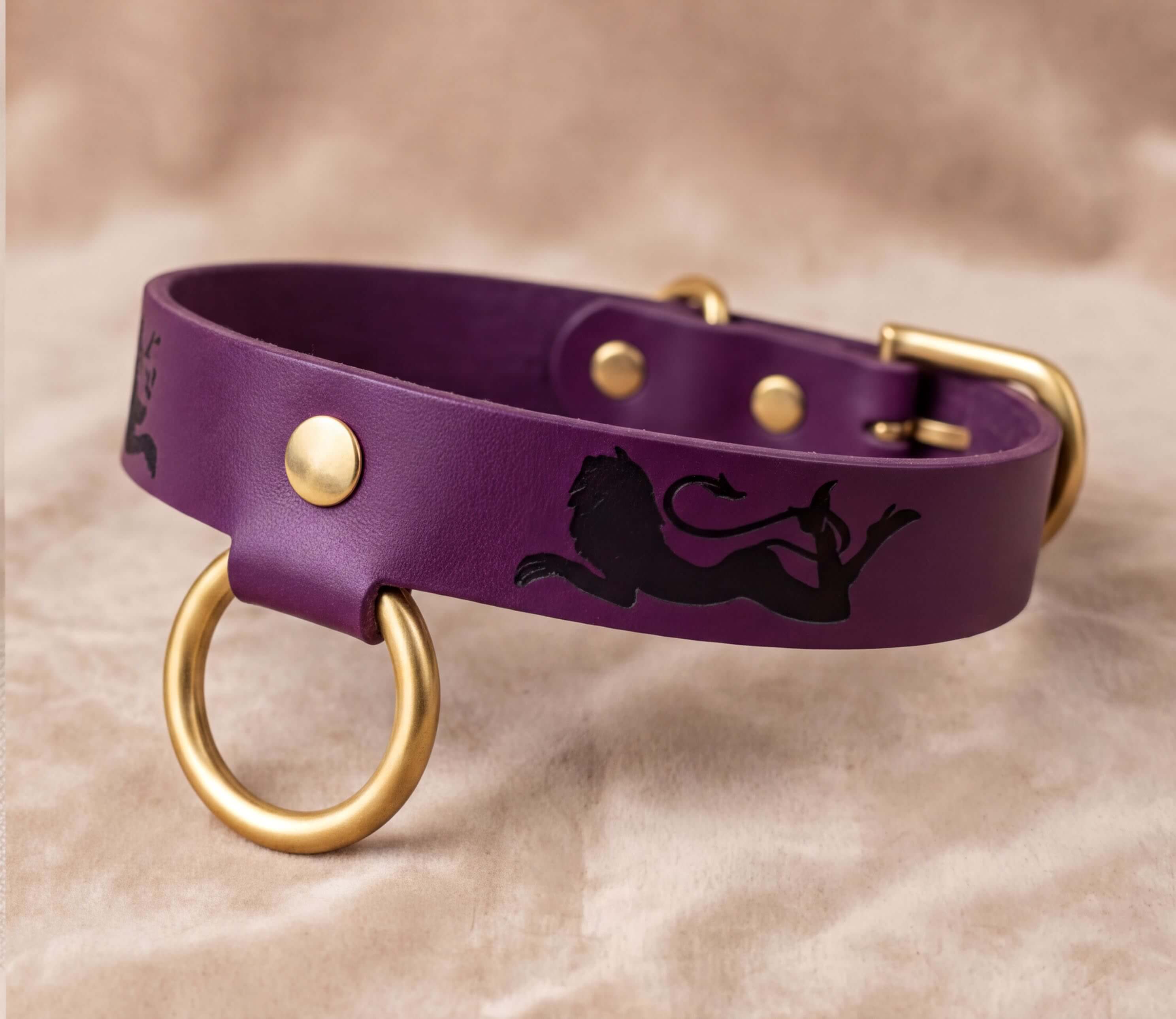 A purple leather dog collar with a lion design and gold-colored metal rings.
