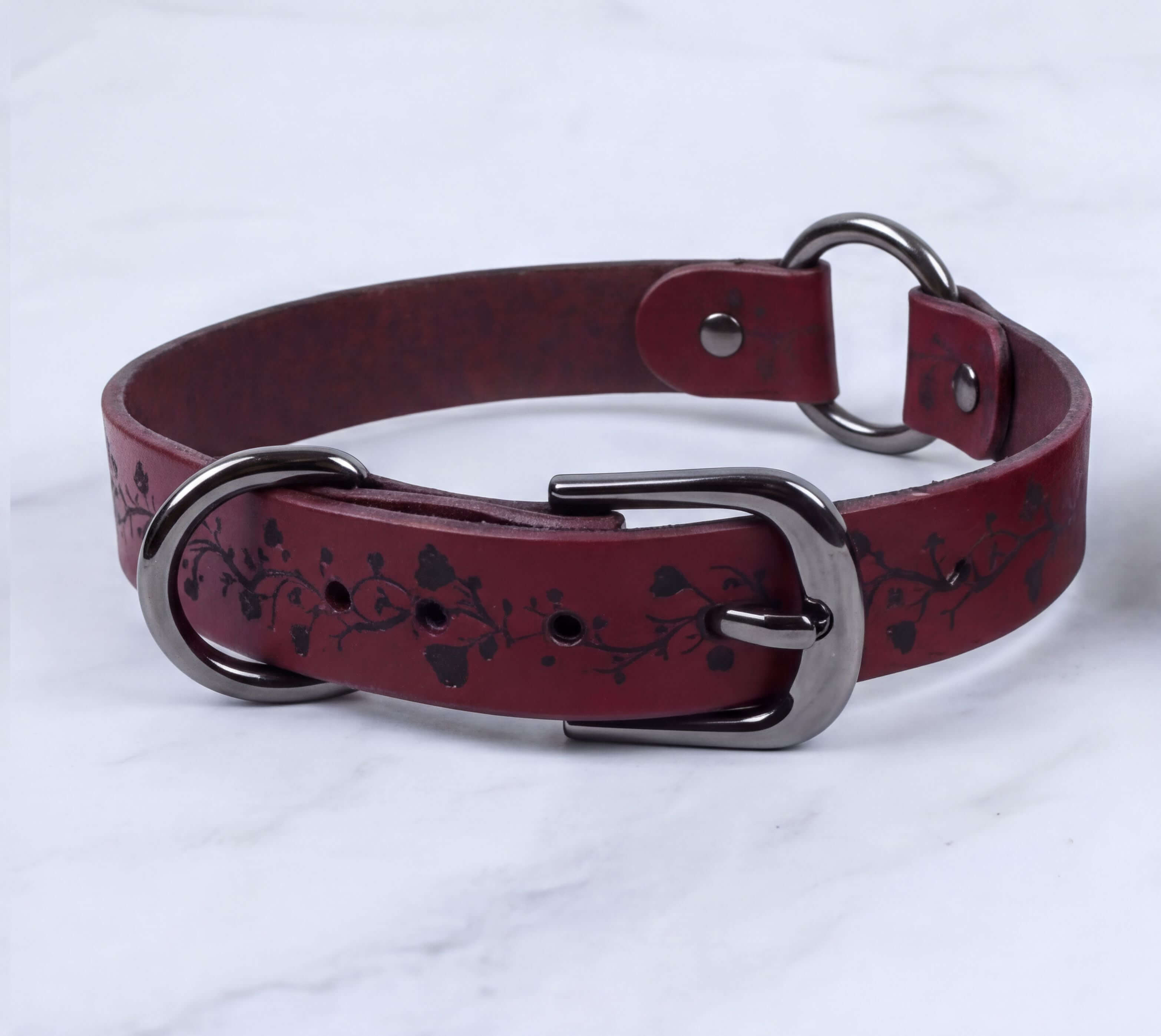 A burgundy leather collar with a metal buckle and two metal rings, one of which is a buckle.