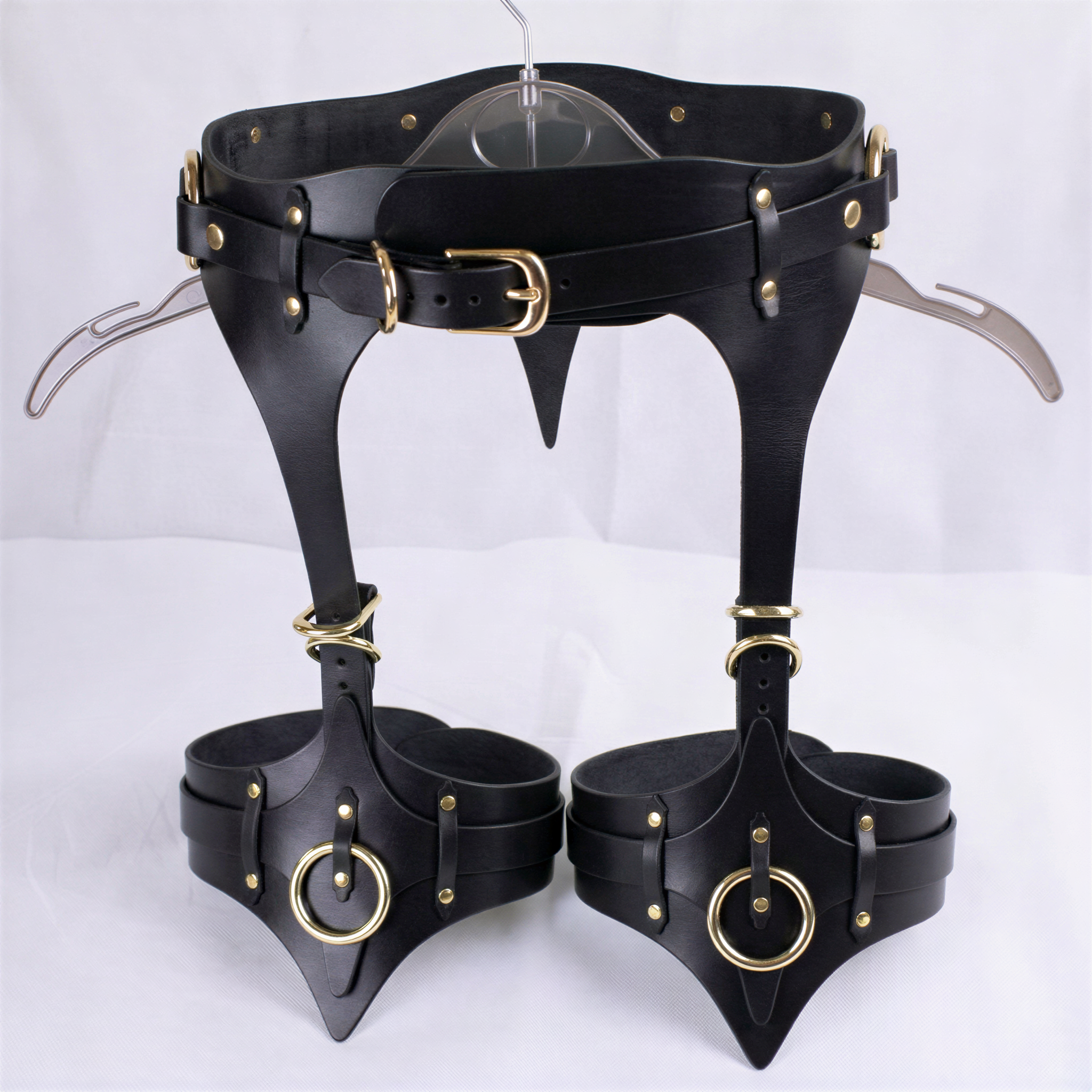 A pair of black leather garter belts with gold-colored buckles and rings, displayed on a white background.