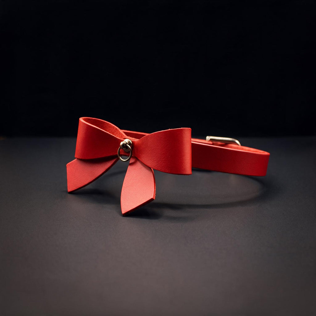 A red bow tie with a gold ring is displayed against a dark background.