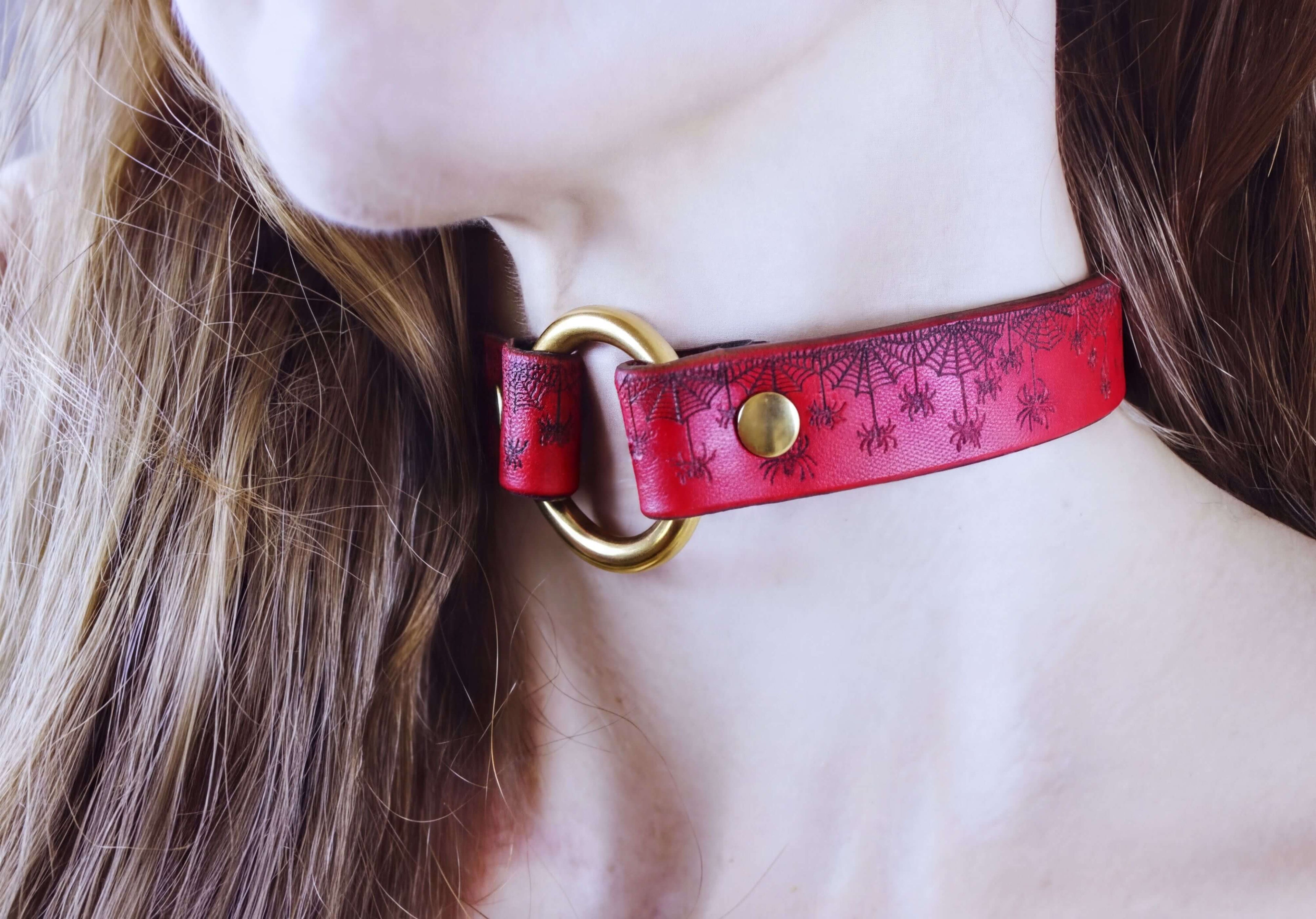 A close-up of a person's neck and chin wearing a red choker necklace with a gold-colored buckle.