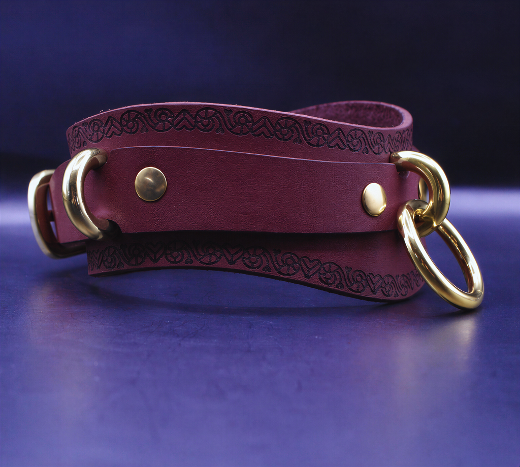 A burgundy leather choker necklace with gold-colored metal rings and a decorative pattern on the clasp.
