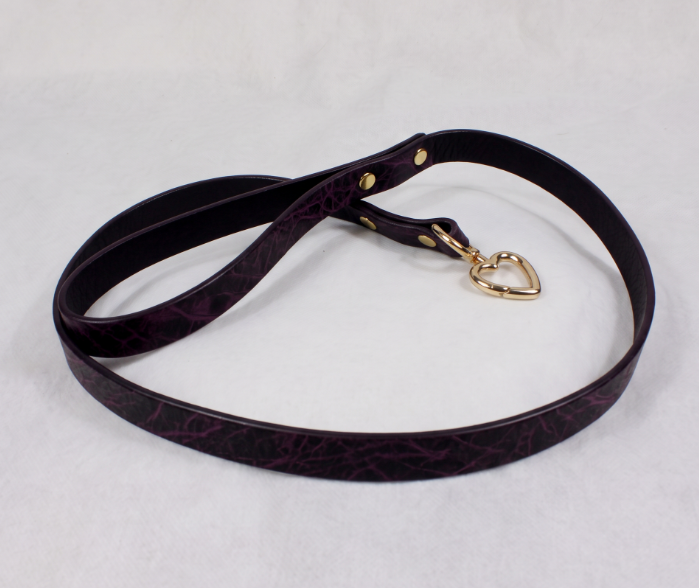 A purple leather leash with a gold heart-shaped tag attached, lying on a white surface.