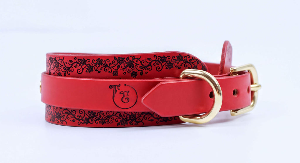 A red leather belt with a decorative floral pattern and a gold buckle.