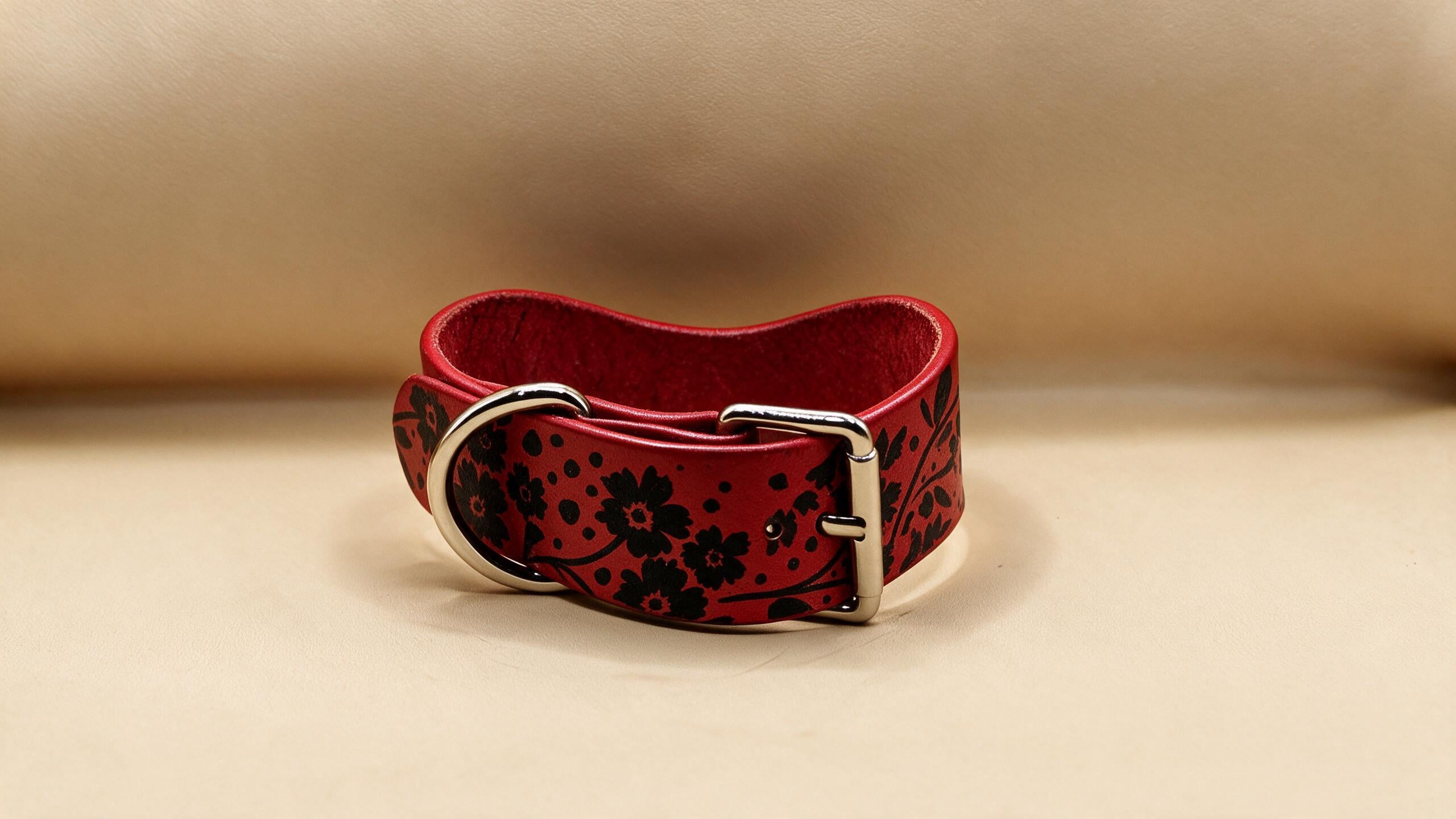 A red leather belt with a floral pattern on it, placed on a beige surface.
