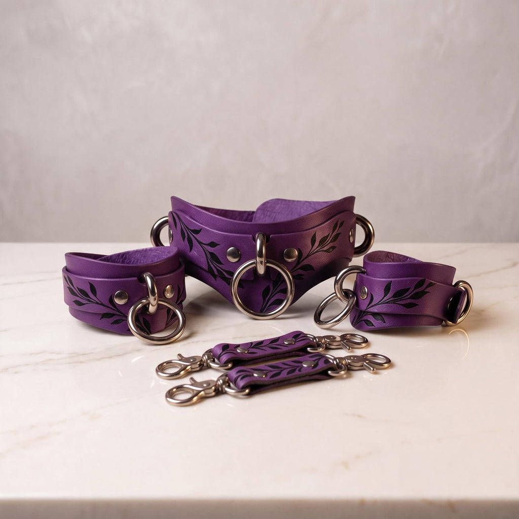 A set of purple leather straps with metal rings and leaf-like designs, arranged on a white marble surface.