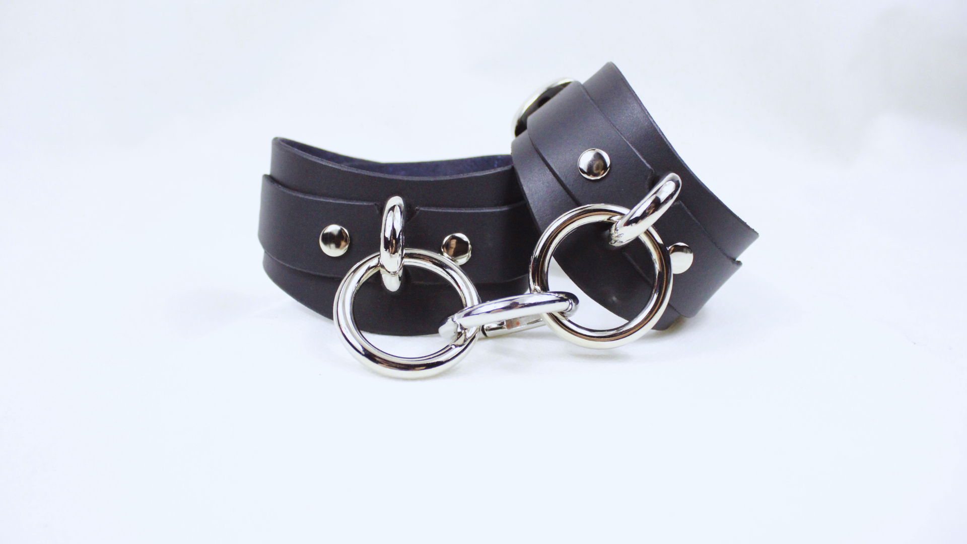 A pair of black leather straps with silver metal rings and buckles, arranged on a white background.