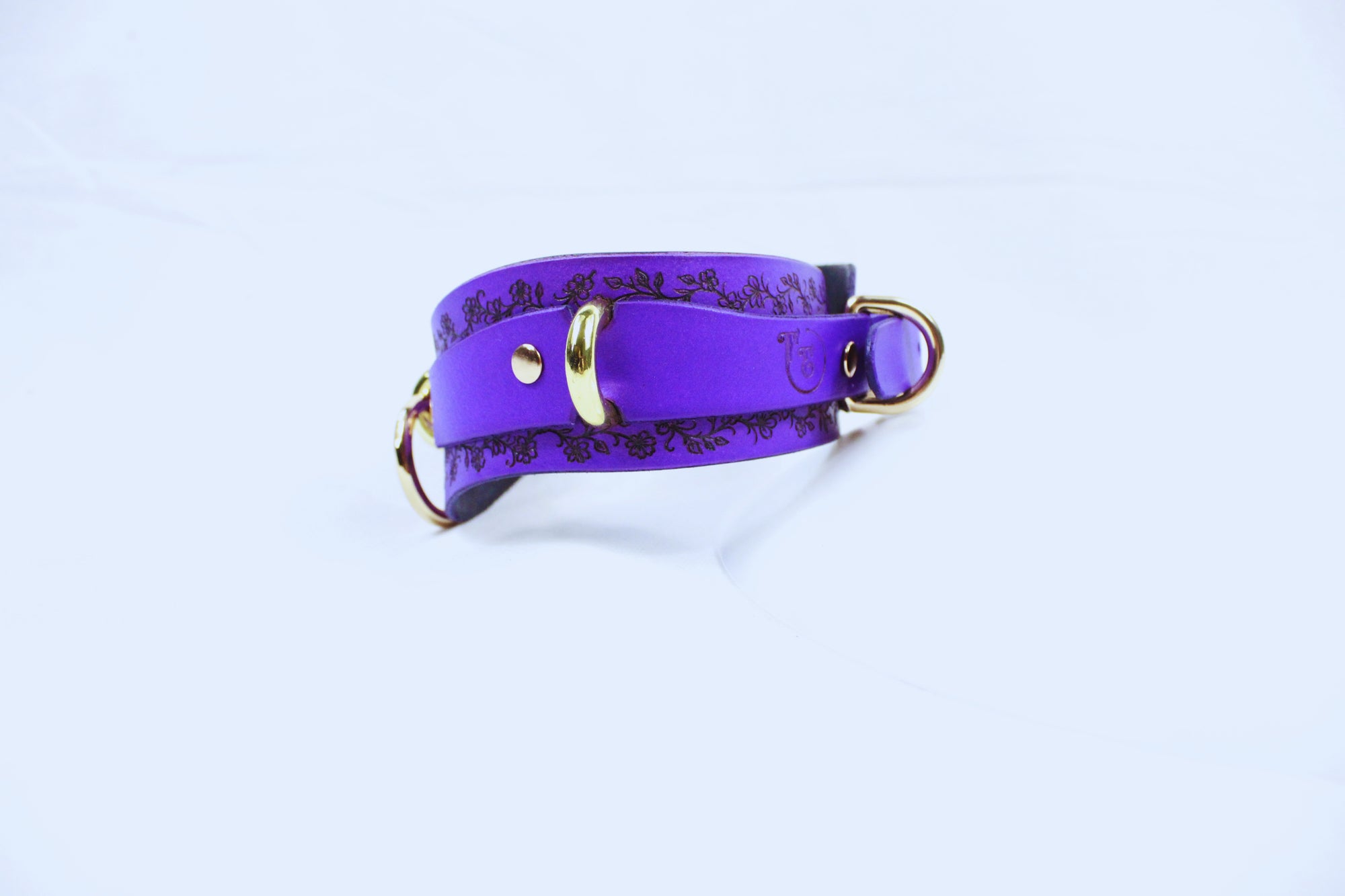 A purple leather collar with a gold buckle and a decorative pattern on the edges.