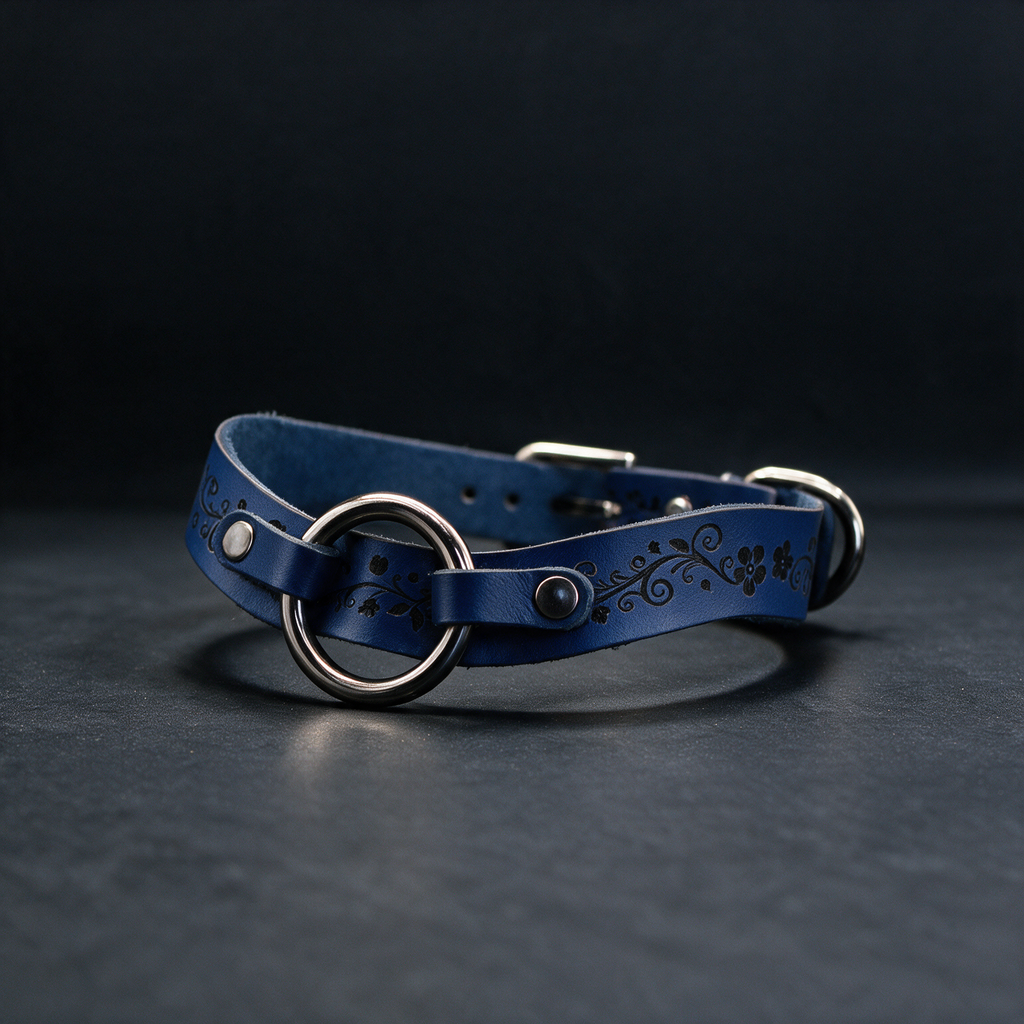 A blue leather collar with a metal ring and decorative elements is displayed against a dark background.