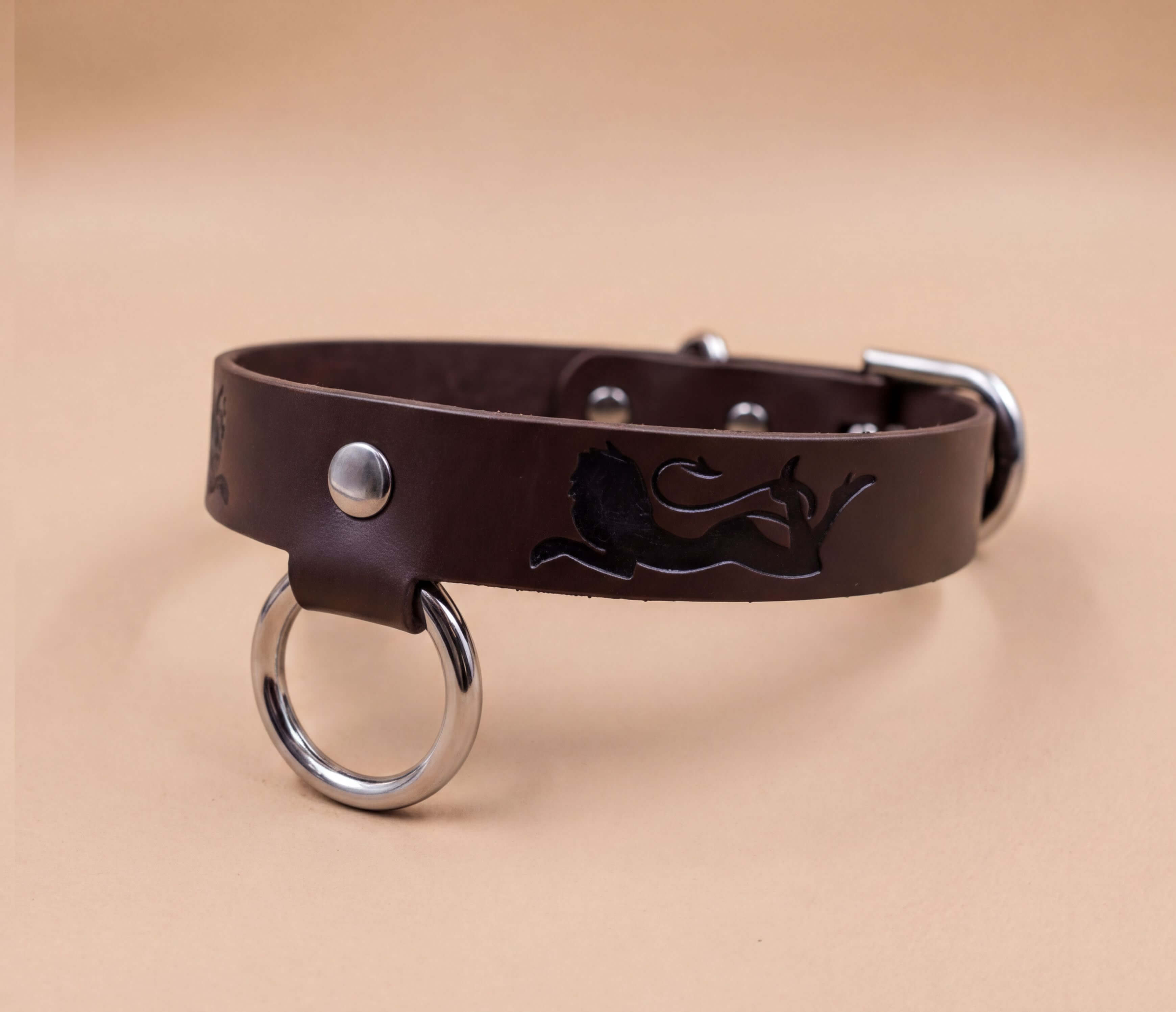 A brown leather dog collar with a metal ring and a lion design on it.