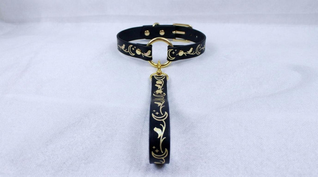 A black collar with a gold-colored metal clasp and a decorative metal tag hanging from it.
