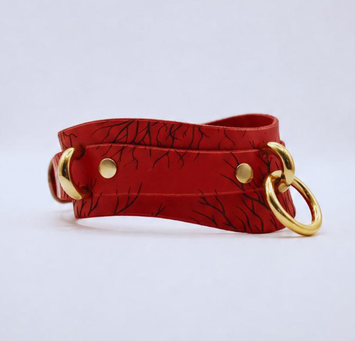 A red leather strap with a black leaf pattern and two gold-colored metal rings on either side.