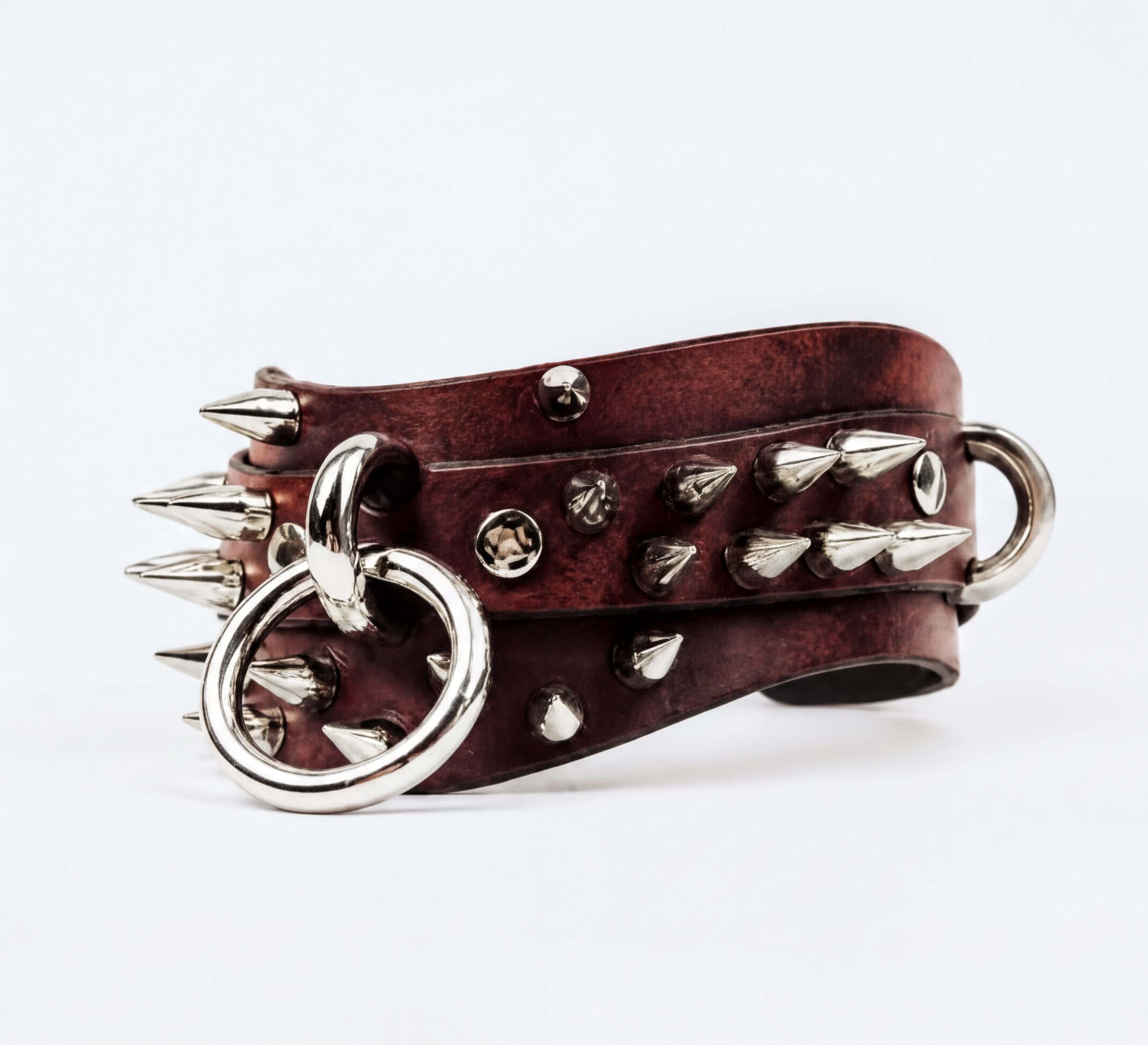 A brown leather strap with silver spikes protruding from it, and a metal ring attached to the strap.