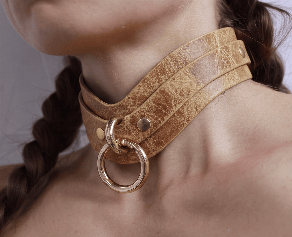 A close-up of a person's neck wearing a tan leather choker necklace with a gold ring.