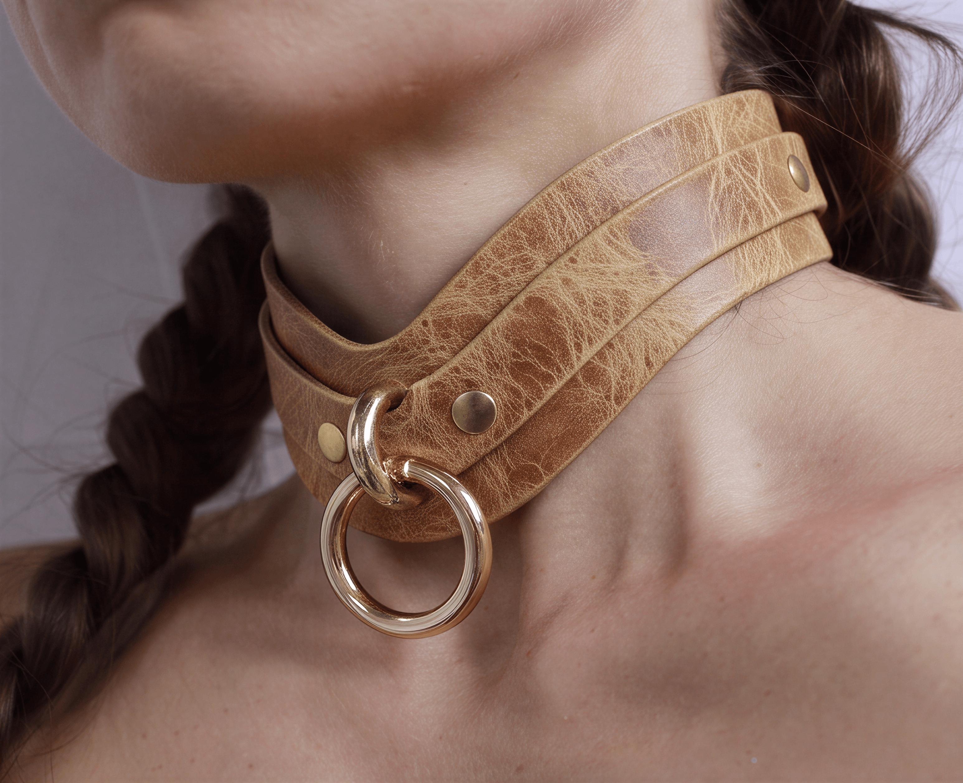 A close-up of a person's neck wearing a tan leather choker necklace with a gold ring.