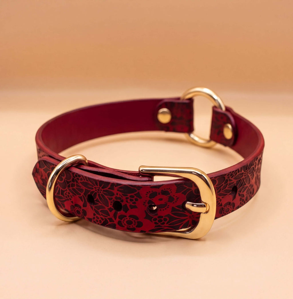 A burgundy leather collar with a floral pattern and a gold buckle.
