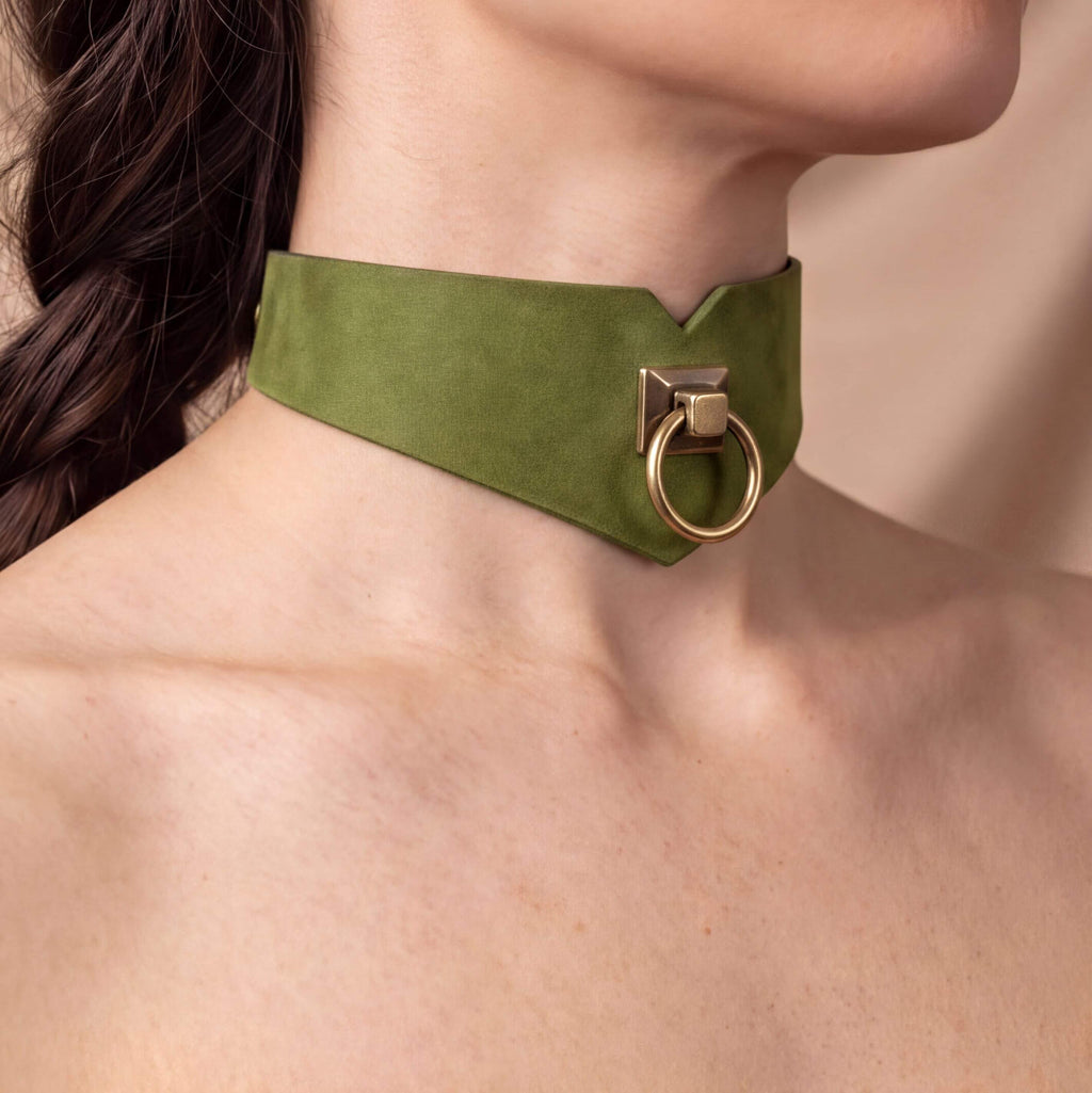 A close-up view of a person's neck and chest area wearing a green choker necklace with a gold-colored metal ring.