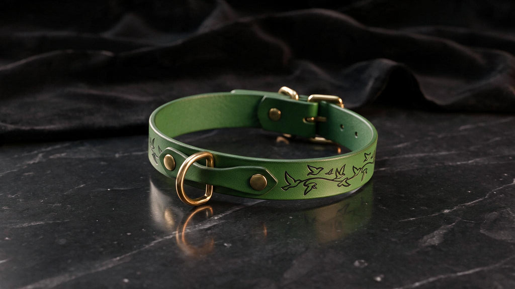 A green leather collar with a gold buckle and a bird design on it, resting on a black marble surface.