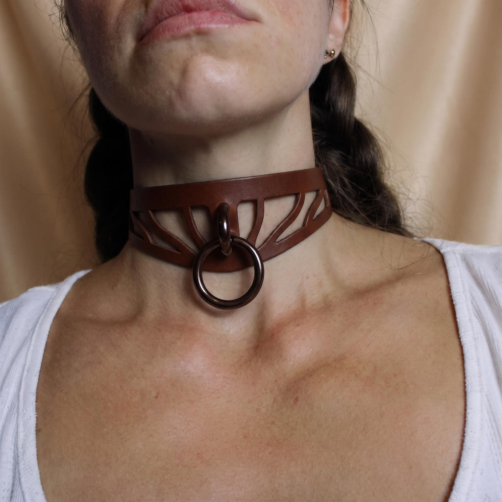 A close-up of a woman's neck and chest area wearing a brown leather choker necklace with a circular ring.